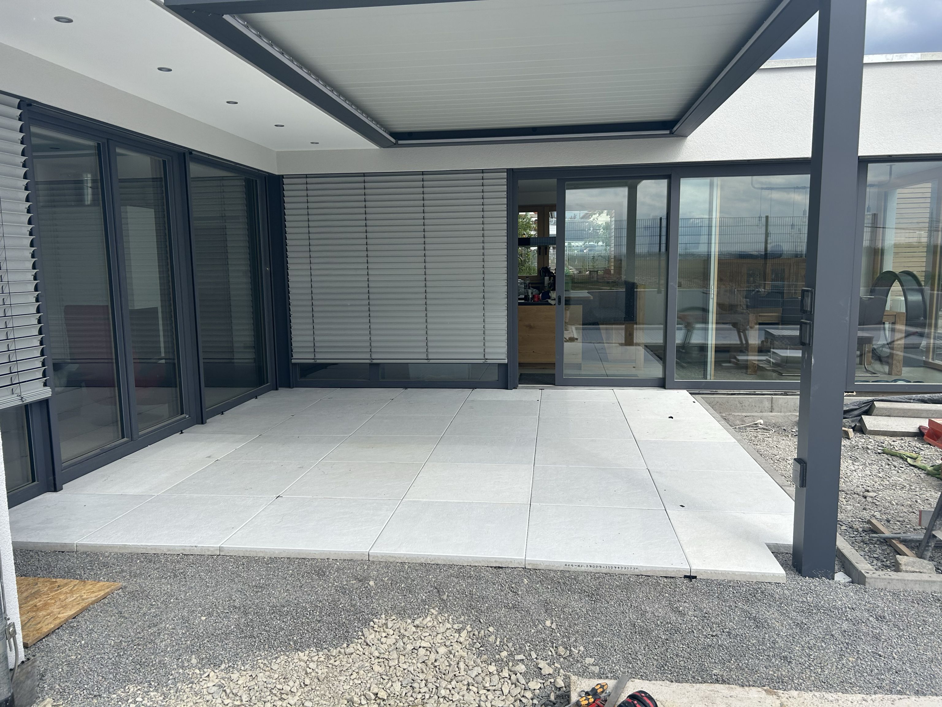 Moderne Terrasse mit großformatigen hellen Platten unter Pergola