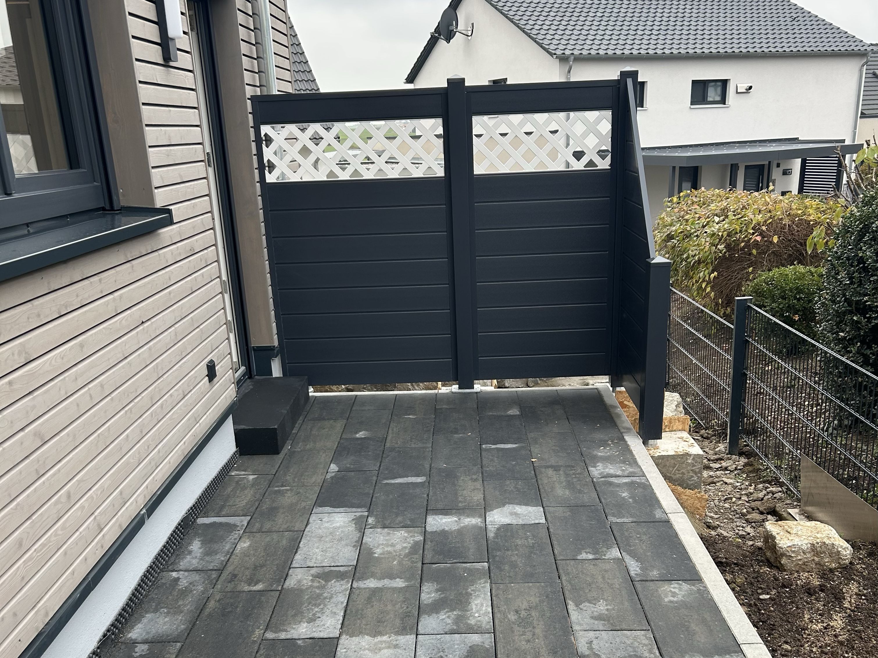 Terrasse mit anthrazitfarbenen Betonplatten und modernem Sichtschutzzaun